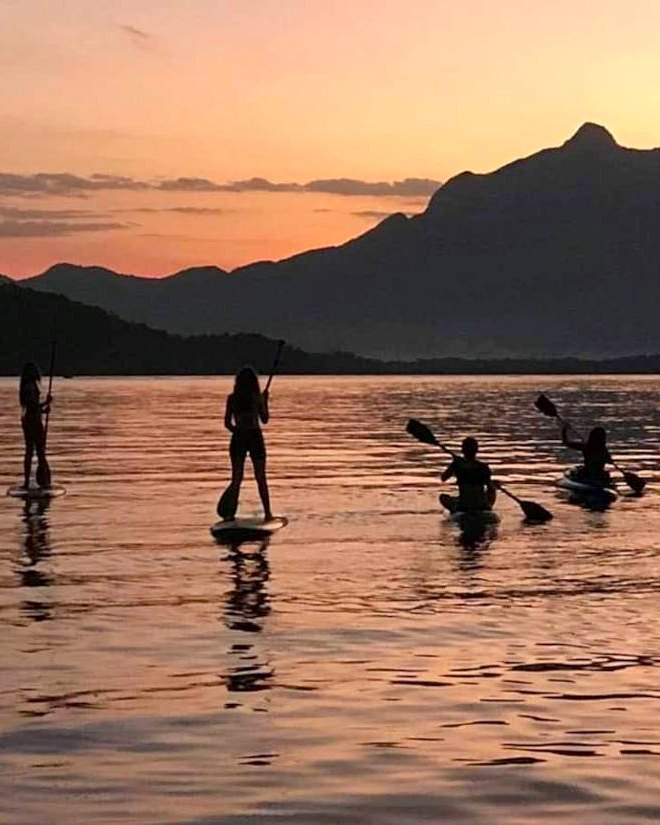 Hóspedes remando de stand up paddle e caiaque em frente à casa ao pôr do sol